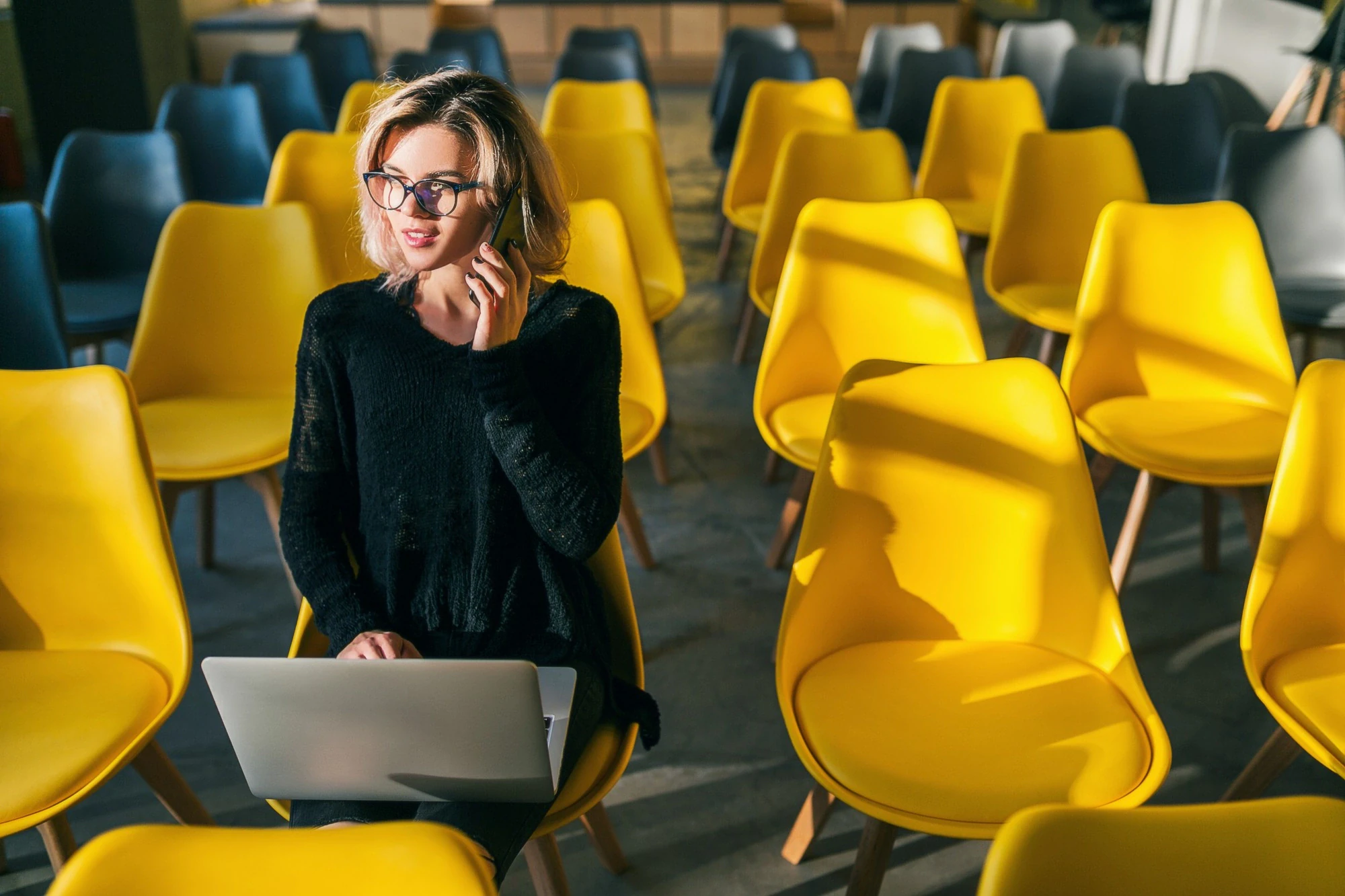 Salesperson on a call with a laptop on their lap among yellow chairs